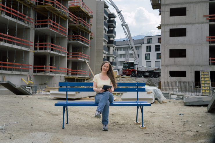 Frau auf der hypoblauen Parkbank inmitten einer Großbaustelle für neue Wohnungen, die mit dem WohnRaum-Kredit mit Wohnbauförderung finanziert werden können.