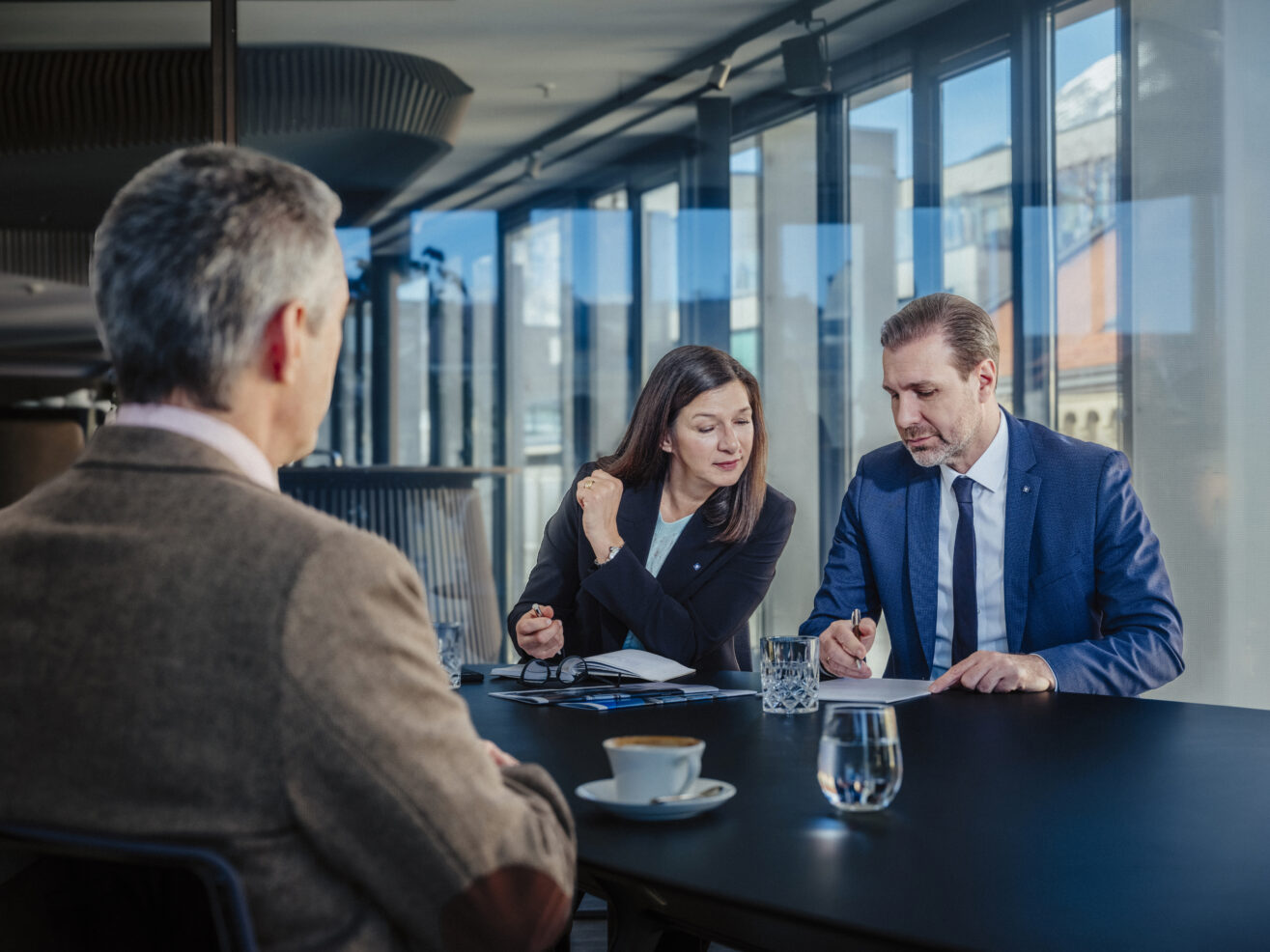 Zwei Berater besprechen Unterlagen mit einem Kunden bei einem Termin im Büro