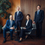 Vorstände und Aufsichtsratvorsitzender der Hypo Tirol posieren zusammen. Der Hintergrund ist eine Holztäfelung, links steht eine Pflanze.